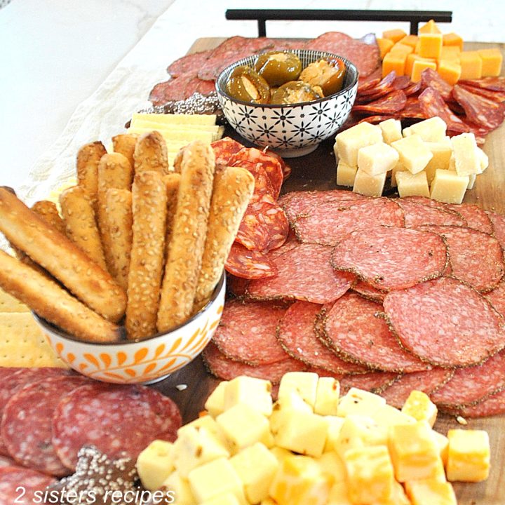 A charcuterie board filled with meats, cheeses, bread sticks and olives,