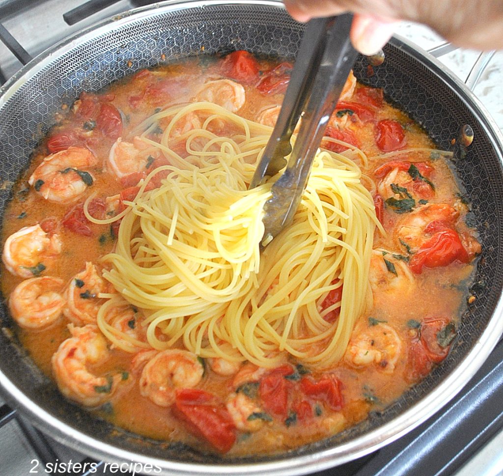 Spaghetti is added to a skillet with cooked shrimps.