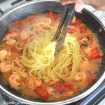 Spaghetti is added to a skillet with cooked shrimps.