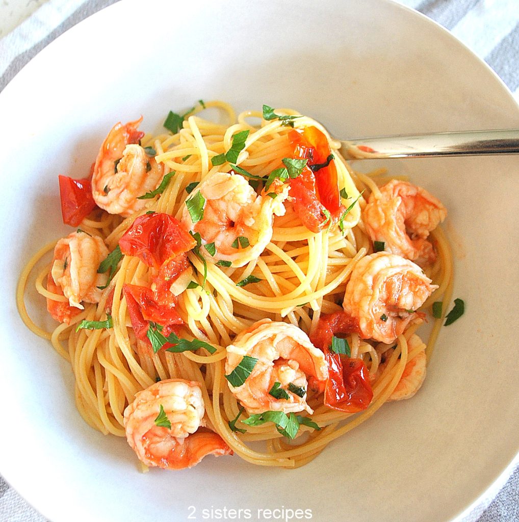 A white bowl filled with spaghetti and shrimp and tomatoes.