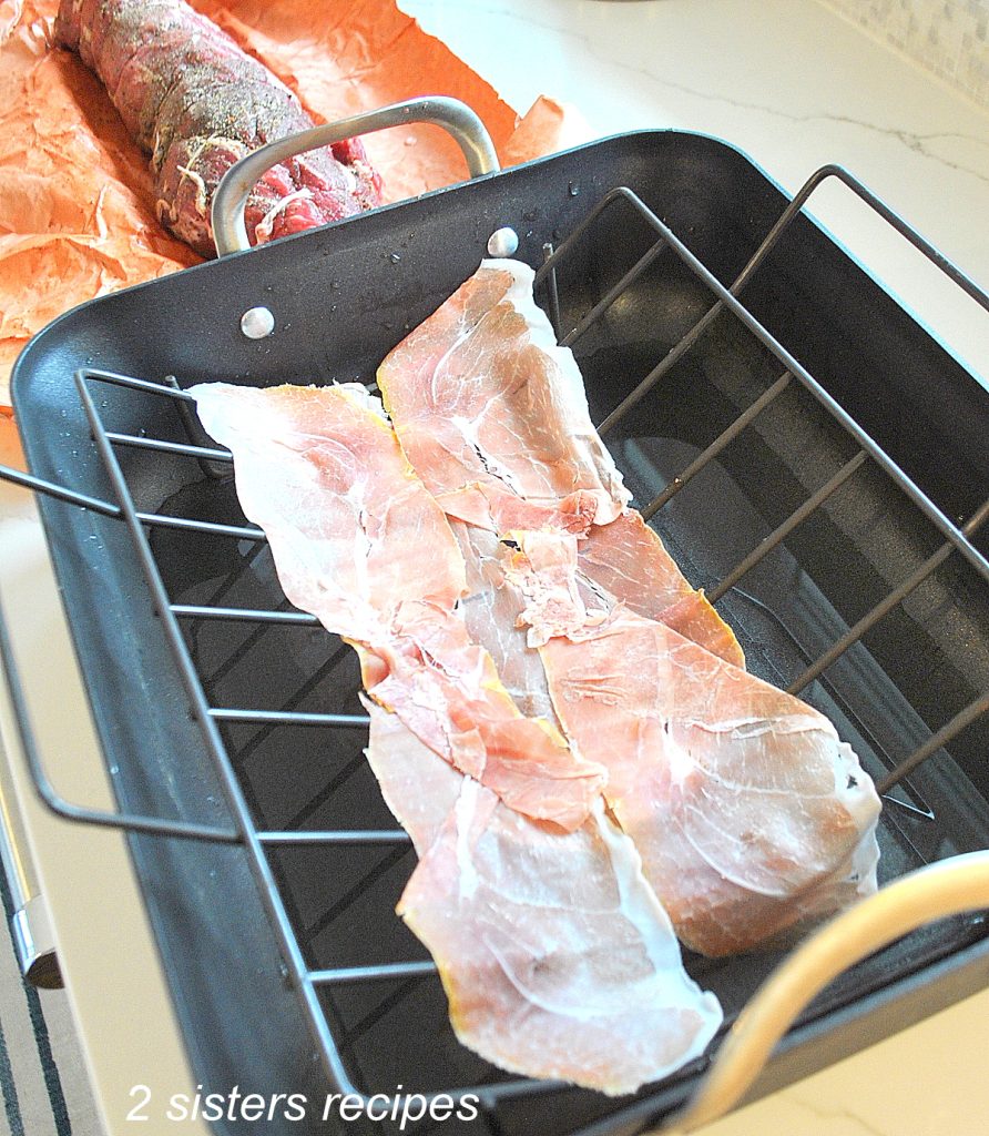 Prosciutto slices are laid on the rack in the roasting pan. by 2sistersrecipes.com