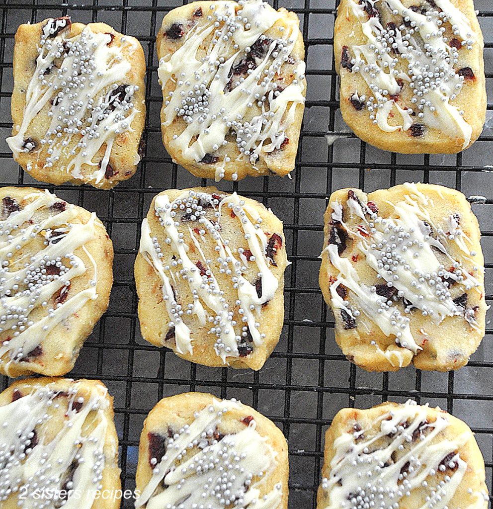 A wire rack filled with baked cookies drizzled with white chocolate and silver beads