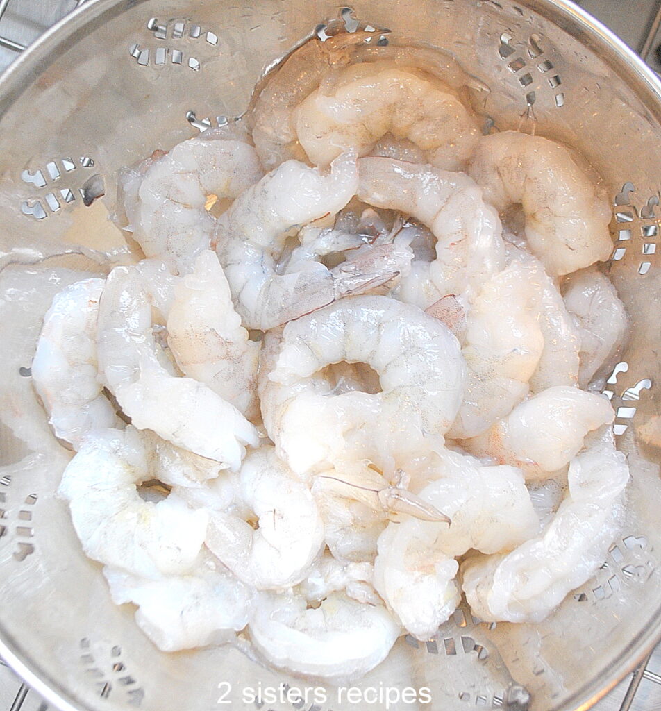 A colander filled with raw, cleaned shrimps.
