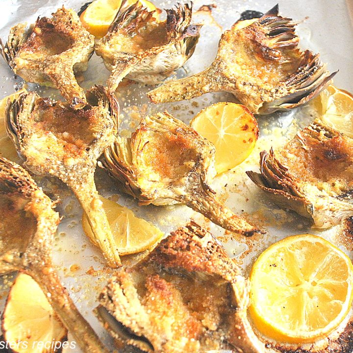 A baking sheet lined with aluminum foil filled with hearts of artichokes and lemon slices.