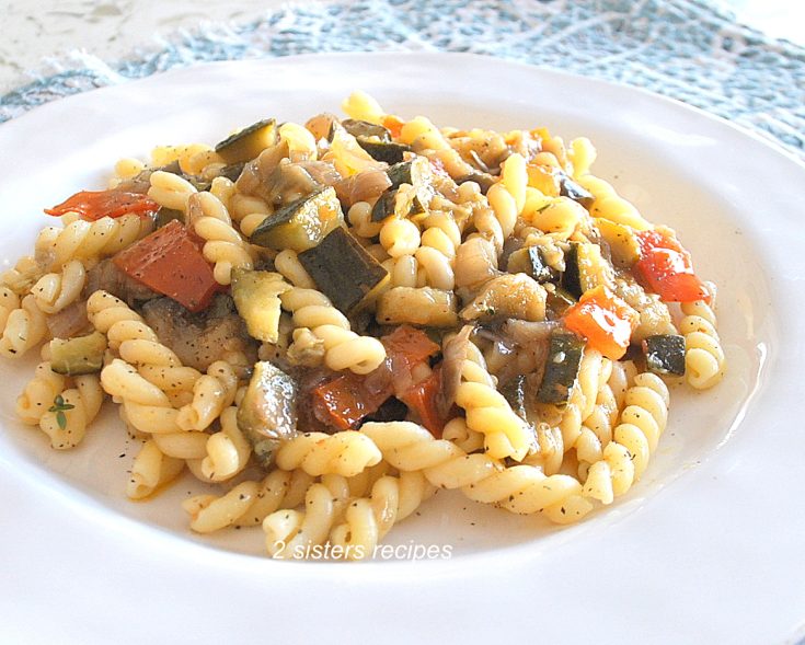 A white dinner plate with curly pasta and veggies.