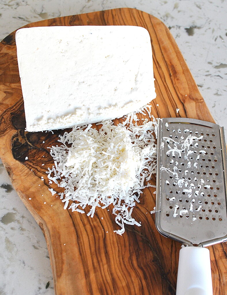 A wood cutting board with a solid block of cheese, grated.