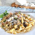 A white plate filled with curly pasta and veggies and grated cheese on top.