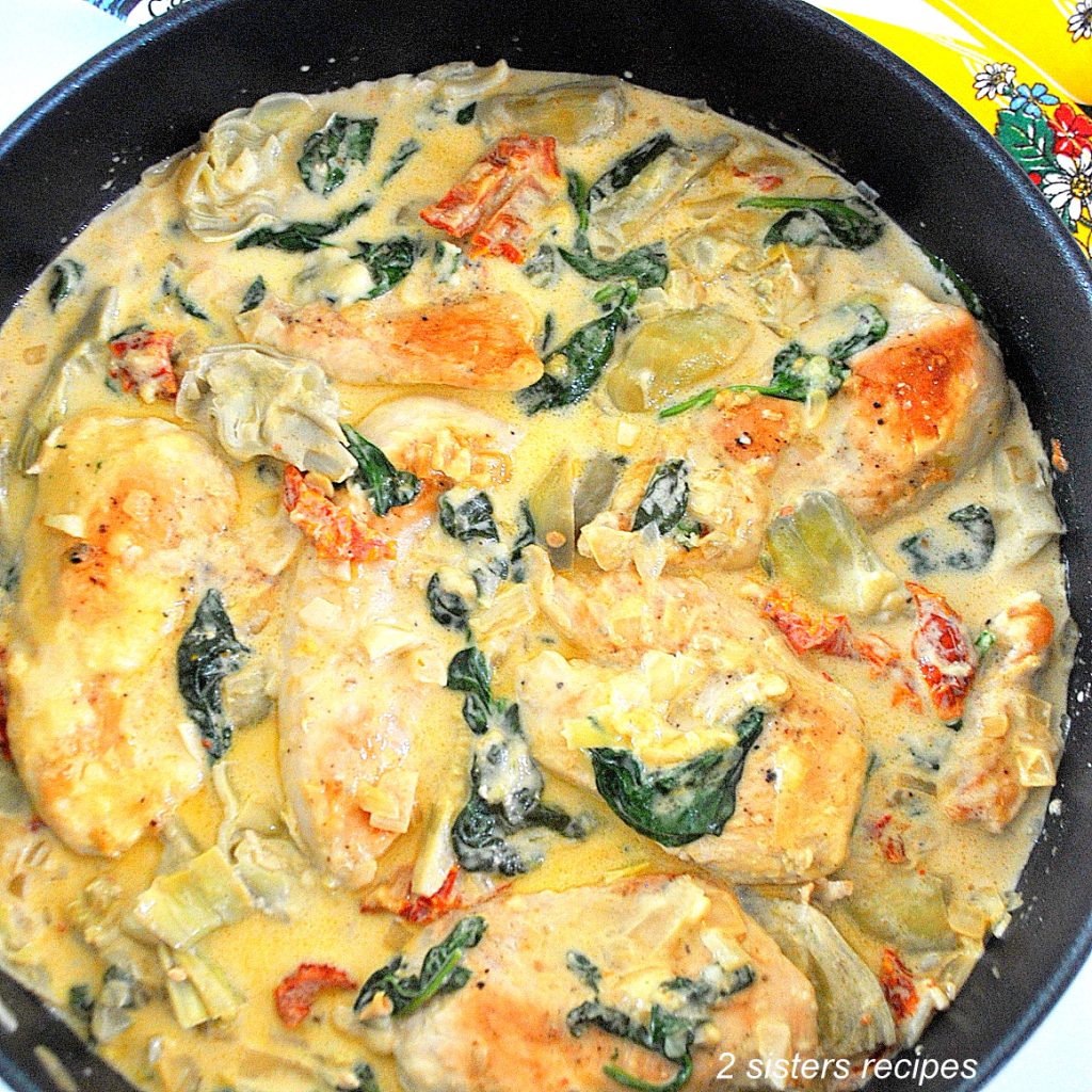 A large black skillet filled with pieces of cooked chicken, veggies smothered in a cream sauce.