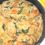 A black skillet filled with cooked chicken and vegetables smothered in a cream sauce.
