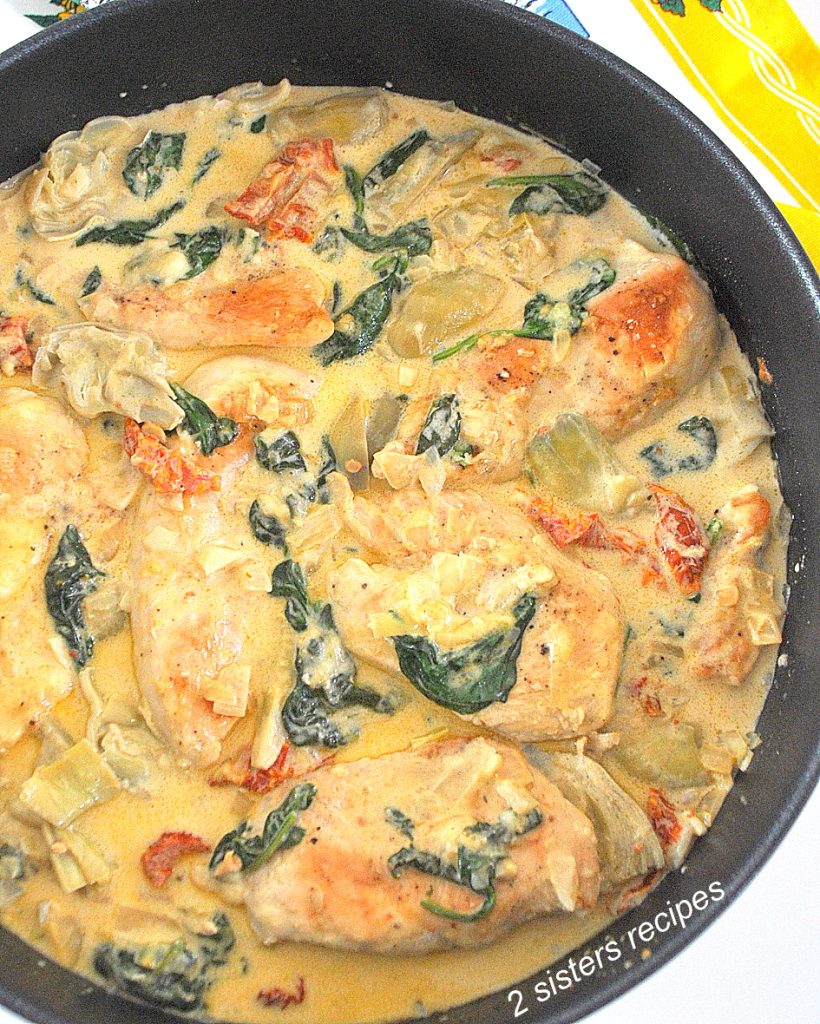 A black skillet filled with cooked chicken and vegetables smothered in a cream sauce.