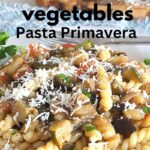 A plate filled with curly pasta loaded with sauteed fresh vegetables.