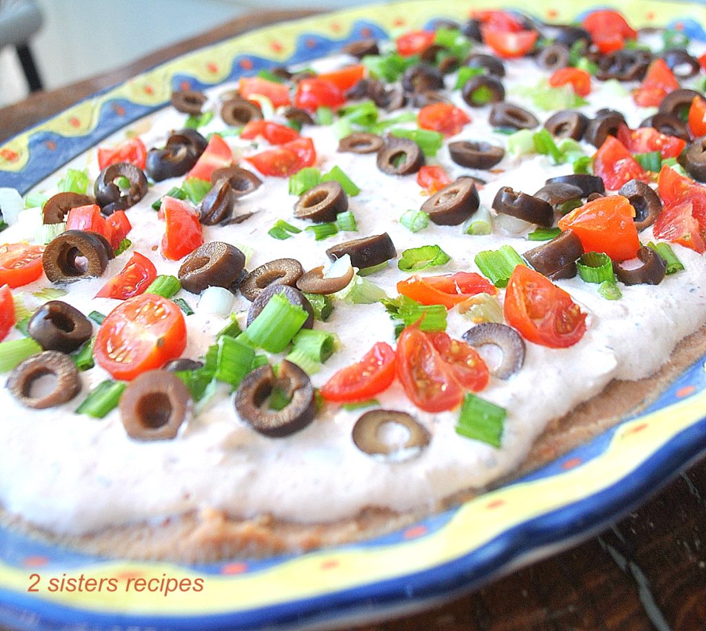 A colorful oval shape platter with creamy mixture topped with chopped green onions, cherry tomatoes and black olives.