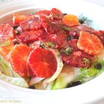 A white plate filled with sliced blood oranges, fennel, capers and raisins.