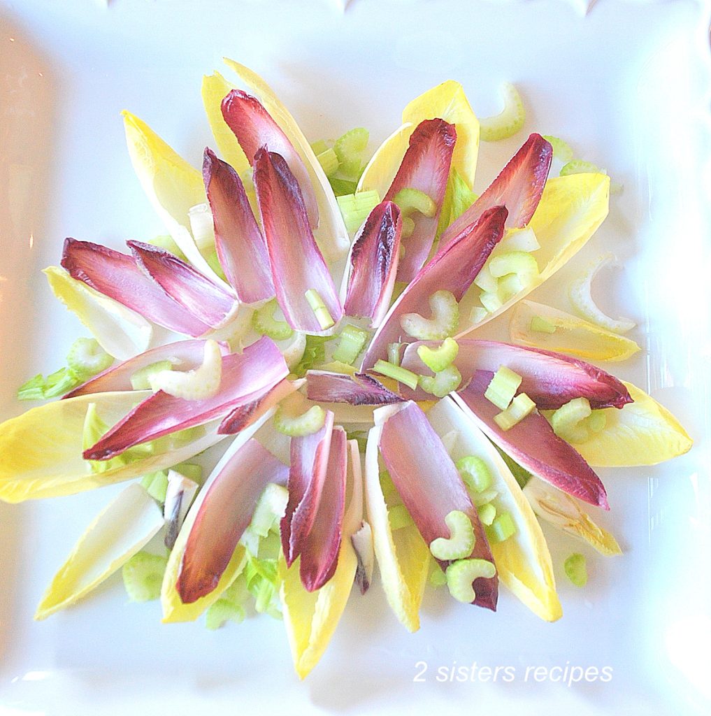 A platter with white and red endive leaves displayed with sliced celery scatter on top.