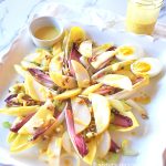 A white square platter with endive leaves, sliced pears, and chopped walnuts on top with dressing over it.