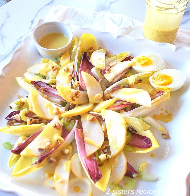 A white square platter with endive leaves, sliced pears, and chopped walnuts on top with dressing over it.