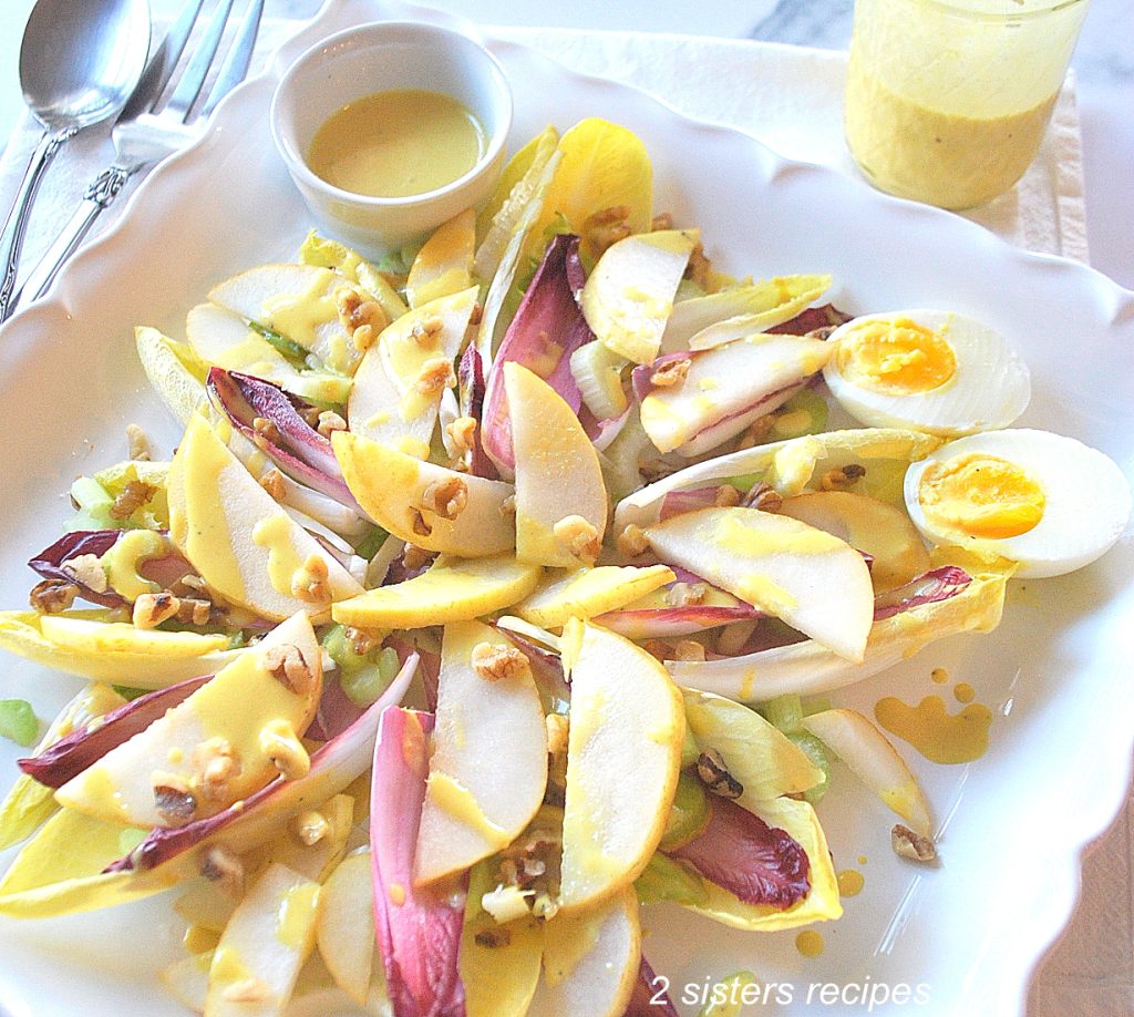 A square platter with endive leaves, sliced pears, hard boiled eggs and dressing on the side.  