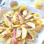 A square platter with endive leaves, sliced pears, hard boiled eggs and dressing on the side.