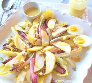 A square platter with endive leaves, sliced pears, hard boiled eggs and dressing on the side.