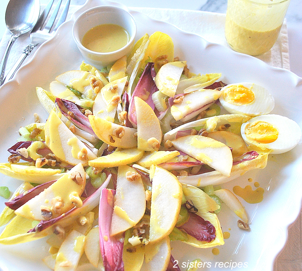 A square platter with endive leaves, sliced pears, hard boiled eggs and dressing on the side.