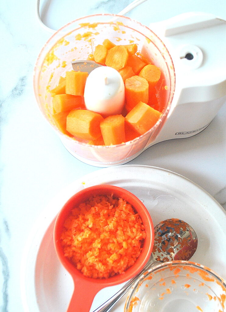 A mini chopper filled with chopped carrots. and a measuring cup filled with minced carrots.