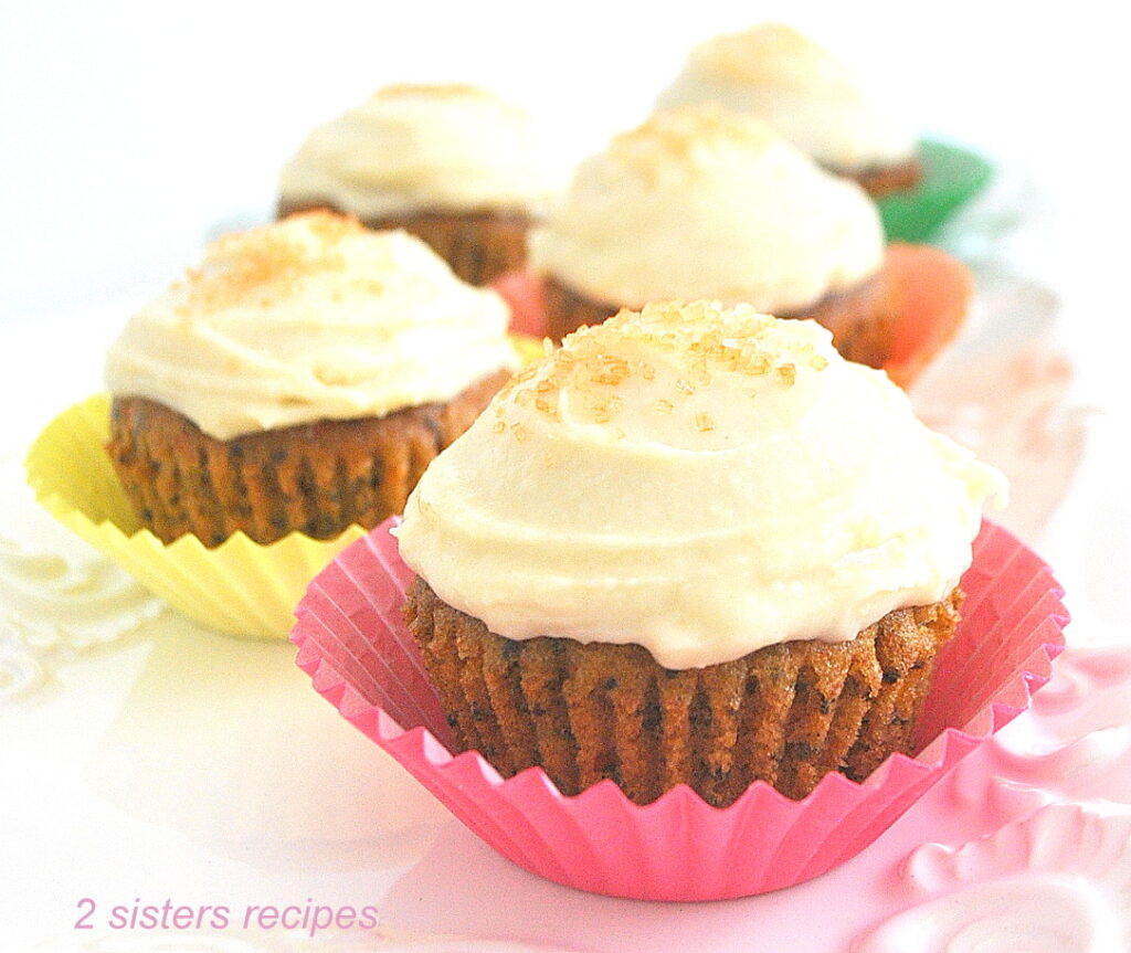 5 cupcakes topped with icing in colorful paper liners on a white platter.