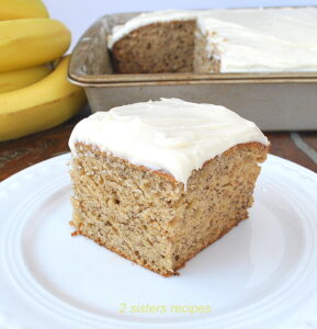 A square piece of banana cake topped with icing on a white plate.