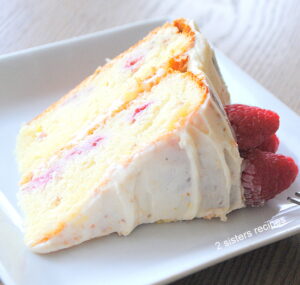 A slice of lemon cake with frosting on top and fresh raspberries