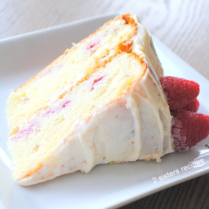A slice of lemon cake with frosting on top and fresh raspberries