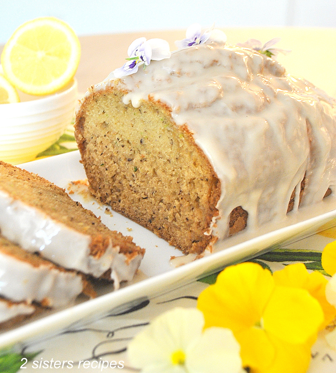 A white serving platter with a quick bread sliced with white icing on top.