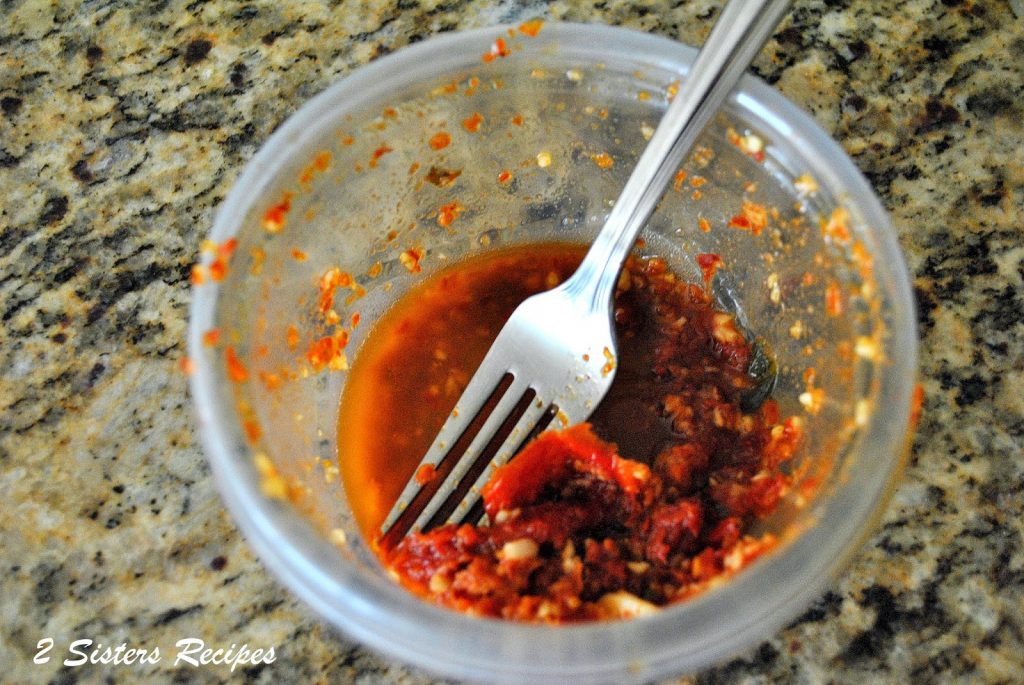 A small plastic container with the sundried tomato and garlic marinade with a fork inside. 