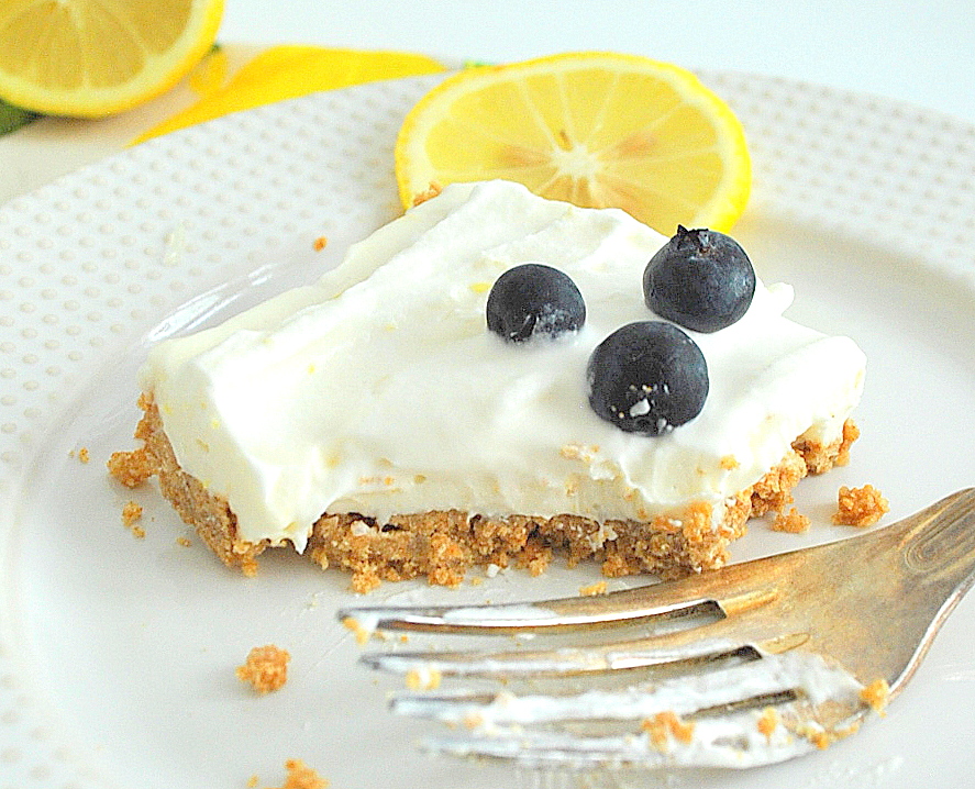 A white plate with a lemon cheesecake bar topped with 3 blueberries and a fork.