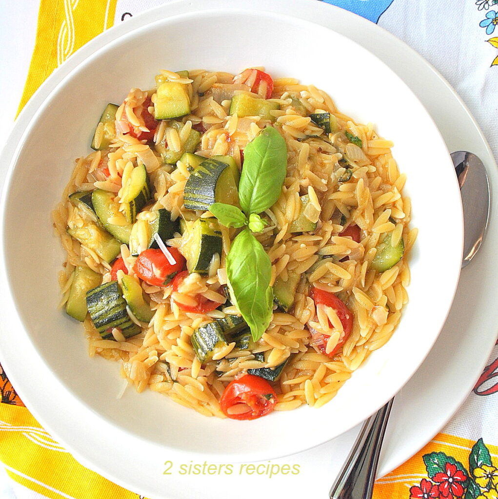 A white plate filled with a serving of orzo pasta, chopped zucchini and cherry tomatoes.