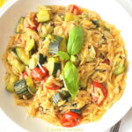 A white plate filled with cooked orzo pasta and vegetables.
