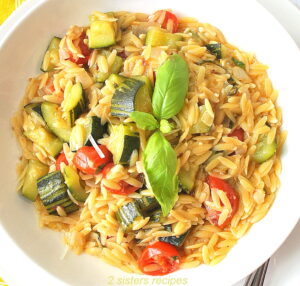 A white plate filled with cooked orzo pasta and vegetables.