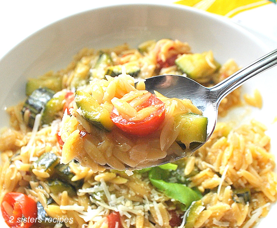 A spoonful of cooked orzo pasta with chopped zucchini and tomatoes.