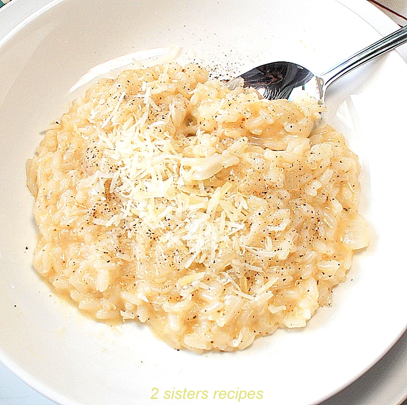 A white dish filled with cooked risotto, topped with black pepper and grated cheese.