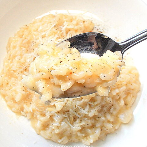 A spoonful of risotto with cheese and black pepper in a white plate.