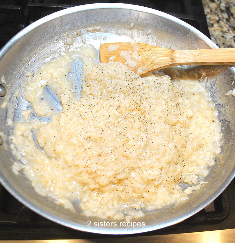 A large stainless steel skillet simmering and stirring the Arborio rice mixture.
