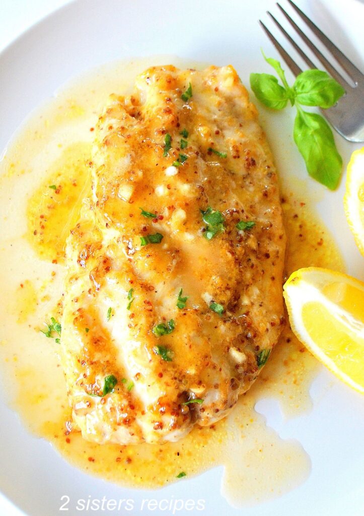 A serving of white fish topped with a glaze and lemon wedge on the side.