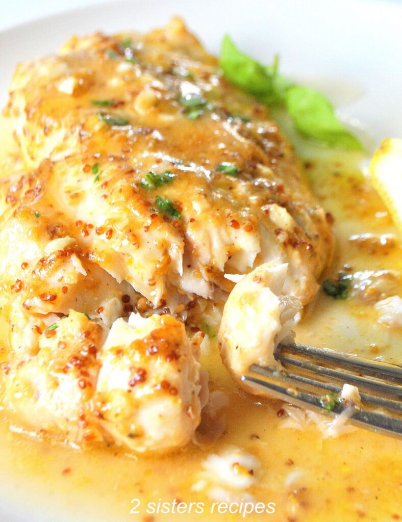 A forkful of white fish baked with a honey mustard glaze on top served on a white plate.