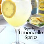 A tall wine glass filled with a limoncello spritz drink, lemon slices and fresh mint on top.