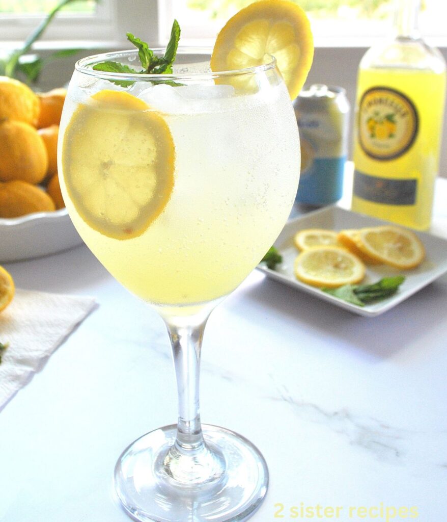 A tall wine glass filled with a lemon spritzer, and lemon slice inside the glass.