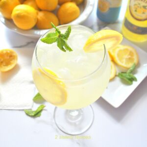 A top view of a wine glass filled with limoncello spritz and lemon slices with fresh mint on top.