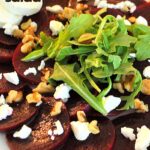 a white plate with sliced beets, arugula, crumbled goat cheese and walnuts.