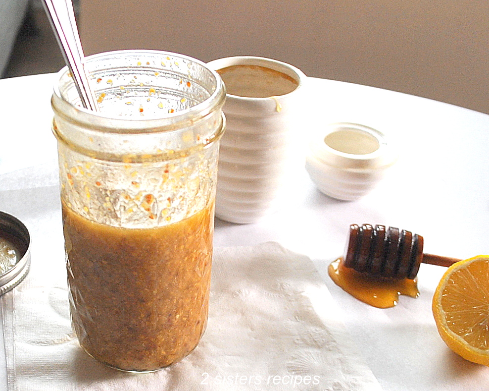 A small mason jar filled with a brownish-color vinaigrette with a spoon inside the jar.