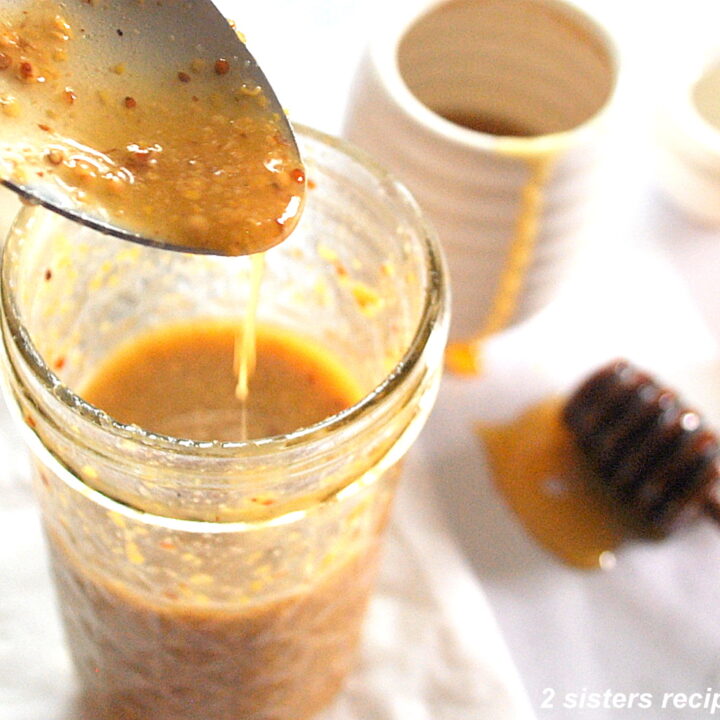 A spoonful of Dijon honey vinaigrette poured back into a mason jar. And a honey stick on the side on the table.