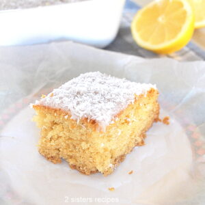A slice of lemon cake topped with shredded coconut served on a white plate.