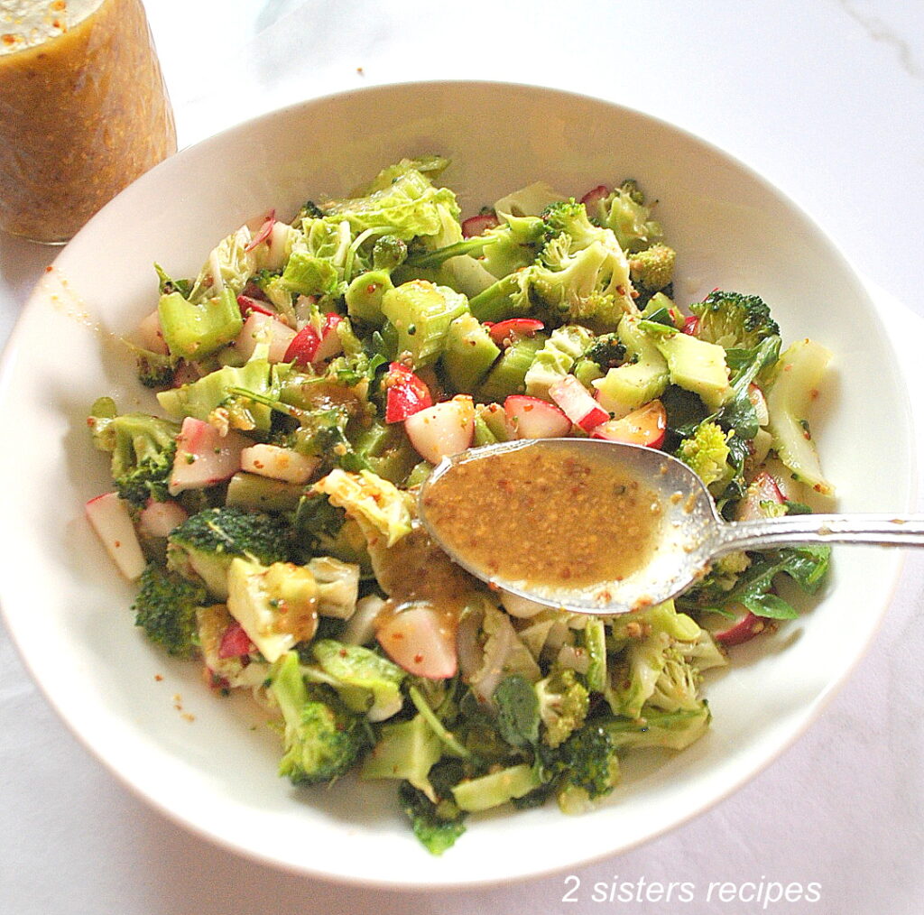 A white bowl filled with a chopped salad, and a spoonful of the Dijon vinaigrette.