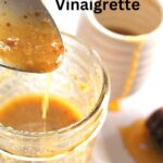 A spoonful of Dijon vinaigrette poured into a small mason jar.